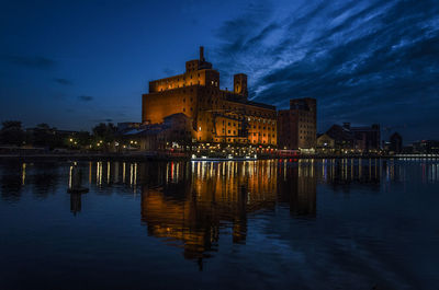 Illuminated buildings by lake against sky at night