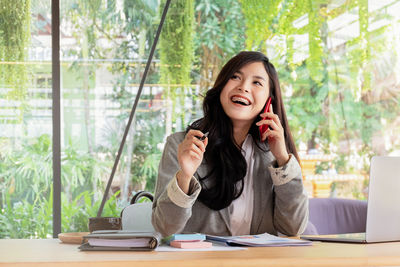 Cheerful businesswoman talking on smart phone while working in office