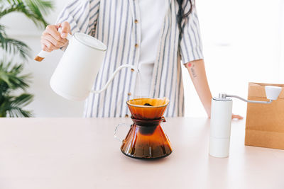 Crop image of professional woman barista hand pouring hot water on ground coffee.