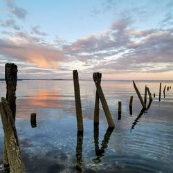 Wooden posts in sea against sky during sunset