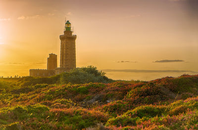 Lighthouse on field against sky during sunset