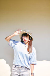 Young woman shielding eyes while standing against wall