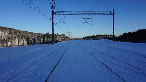 Electricity pylon by railroad tracks against clear blue sky during winter