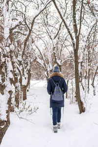 Rear view of woman wearing warm clothing with backpack walking on snow in forest