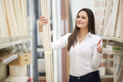 Portrait of smiling young woman showing thumbs up while holding planks in store