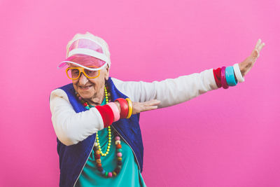 Happy senior woman arms raised dancing against pink background