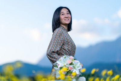 Young woman standing by flowering plants against sky