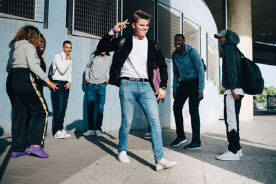 Cheerful friends looking at young man standing on sidewalk in city