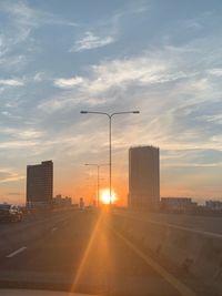 Road by buildings against sky during sunset in city