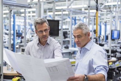 Two businessmen in factory hall discussing construction plan