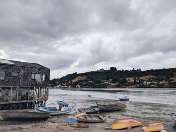 Boats moored on beach by buildings against sky