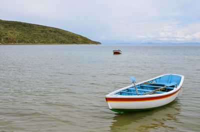 Boat anchored on river by mountain against cloudy sky