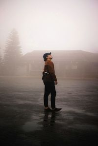 Side view of man looking up while standing on road during foggy weather