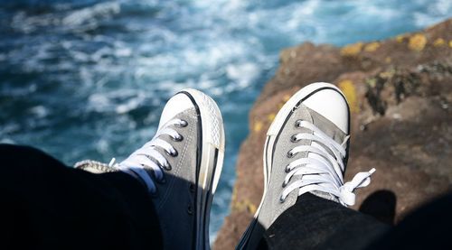 Low section of man wearing canvas shoes on rock at beach