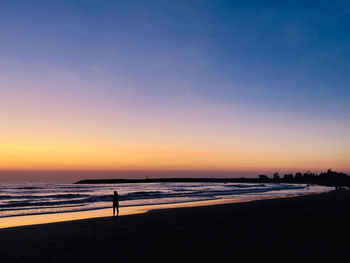 Silhouette people on beach against sky during sunset