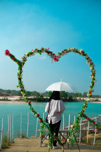 Rear view of woman standing by sea against sky