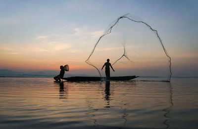 Silhouette people on sea against sky during sunset