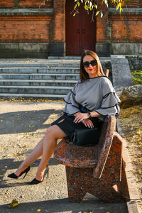 Portrait of young business woman sitting outside. girl in blouse and skirt on high heels. brunette