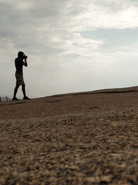 Side view of man photographing on landscape against sky