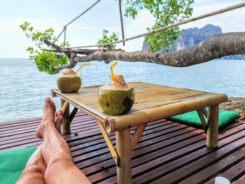 Low section of man relaxing on plank by sea against sky