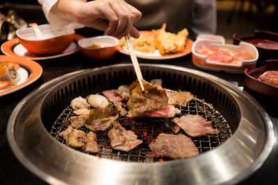 Midsection of woman using chopsticks while picking food from metal grate