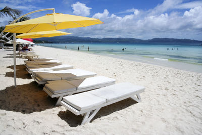 Deck chairs on beach against sky