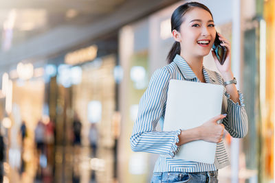 Smiling young woman using phone while standing against blurred background