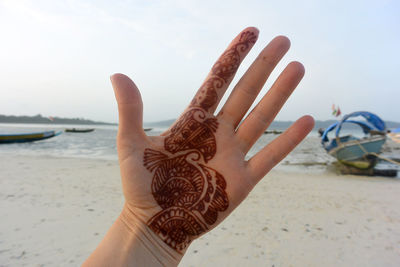 Cropped image of woman with henna tattoo on hand at beach against sky