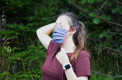 Portrait of young woman with brown ponytail in a colorful patterned face mask on a nature background