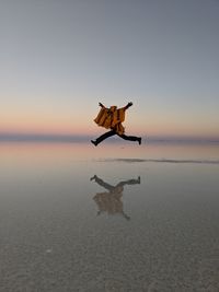 Side view of woman jumping on shore at beach against sky during sunset
