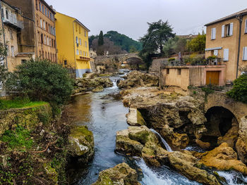 River amidst buildings and trees against sky