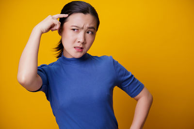 Portrait of young woman standing against yellow background