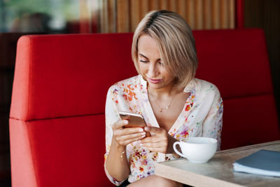 A young woman in a cafe drinks coffee and uses a mobile phone, writes messages