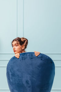 Teen girl posing behind a blue armchair on turquoise background