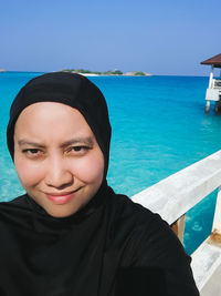 Portrait of smiling woman wearing hijab against seascape