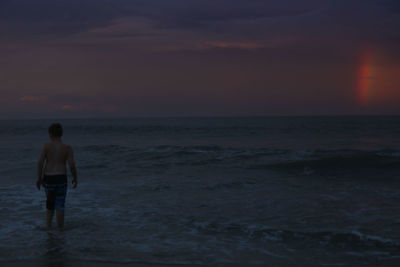 Rear view of man standing on beach against sky during sunset