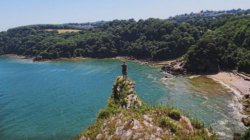 Young man standing on cliff against sea