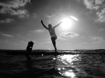 Boy standing in sea against sky during sunset