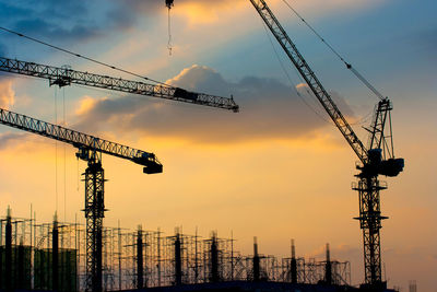 Low angle view of cranes at construction site against sky during sunset
