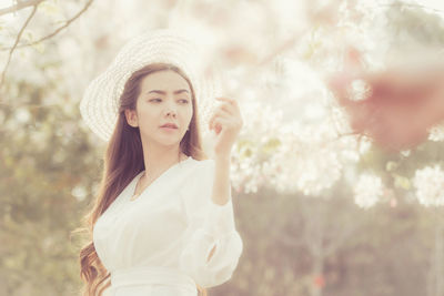 Portrait of beautiful young woman standing against plants