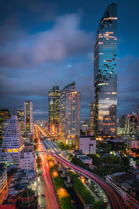 High angle view of light trails on road amidst modern buildings against cloudy sky at night