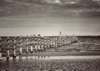 Wooden posts on beach against sky