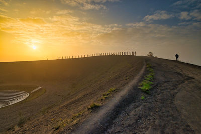 Scenic view of road amidst field against sky during sunset