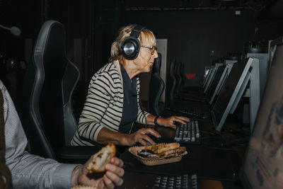 Elderly woman playing video game on computer by male friend at gaming center