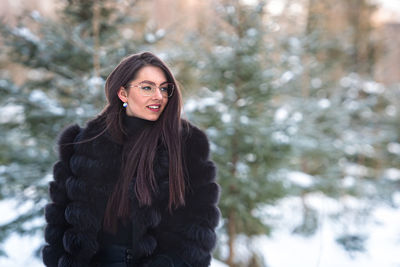 Portrait of smiling young woman standing outdoors during winter