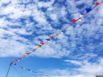 Low angle view of buntings and illuminated light bulbs hanging against sky