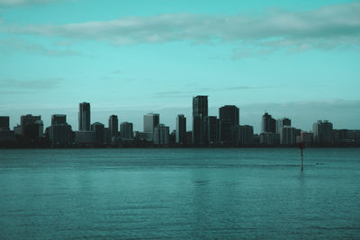 Sea by modern buildings against sky in city