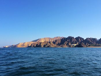 Scenic view of sea and mountains against clear blue sky