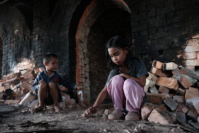 Full length of children sitting on stone wall