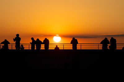 Silhouette people standing by sea against orange sky